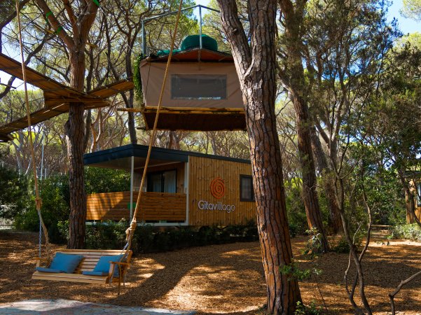 Bungalow in legno tra gli alberi con un’altalena e una tenda sospesa.