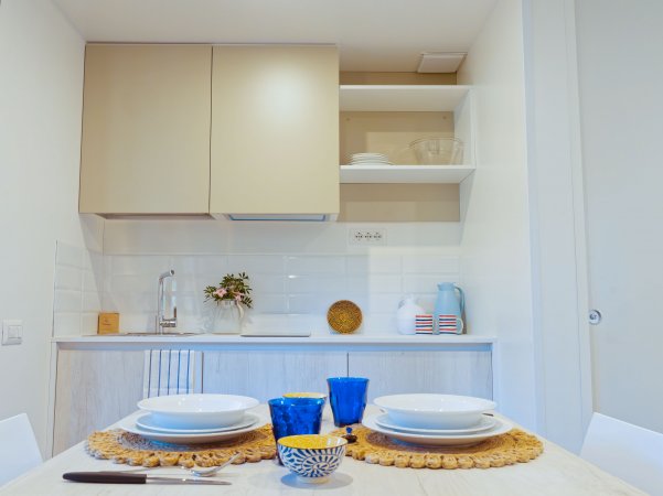 Cucina moderna con tavolo apparecchiato, bicchieri blu e piatti bianchi.