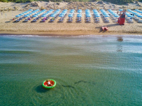 Vista dall'alto di una spiaggia con ombrelloni azzurri e un gonfiabile in mare.