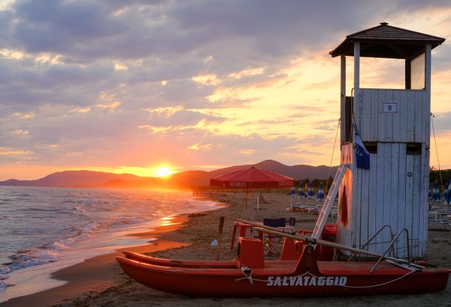 Una torretta di salvataggio su una spiaggia al tramonto, con un gommone rosso.