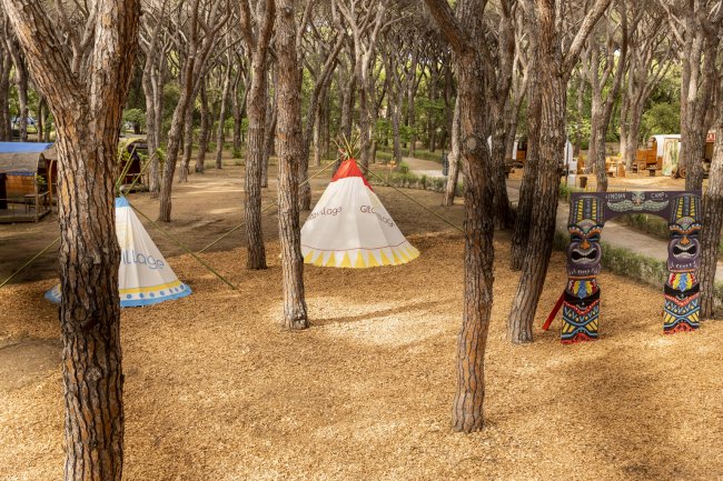 Due tende a forma di tipì colorati tra gli alberi, con totem decorativi su un lato.