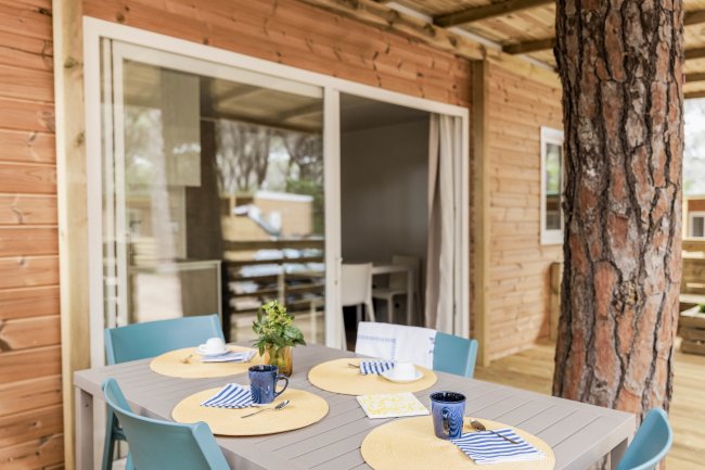 Un tavolo apparecchiato all'esterno di una casa in legno con sedie blu e grandi finestre.