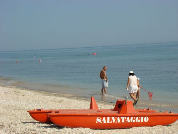 Una spiaggia con un'imbarcazione arancione per il salvataggio e persone che camminano lungo la riva.