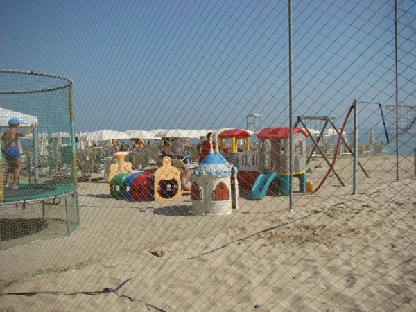 Area giochi sulla sabbia con scivoli e strutture colorate, recintata.