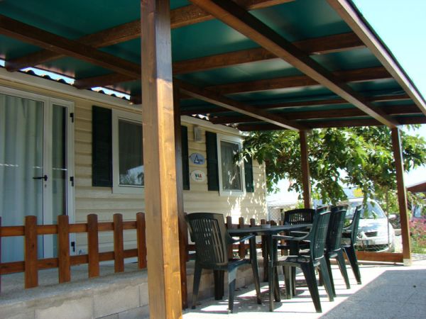Veranda di una roulotte con tavolo e sedie di plastica nera.