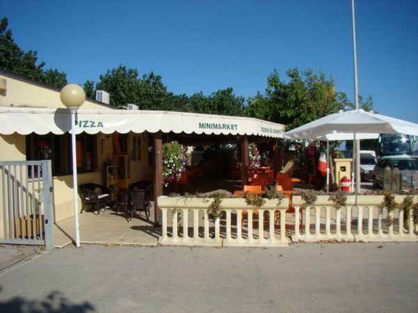 Area esterna minimarket con tenda bianca, tavoli arancioni sotto gazebo.