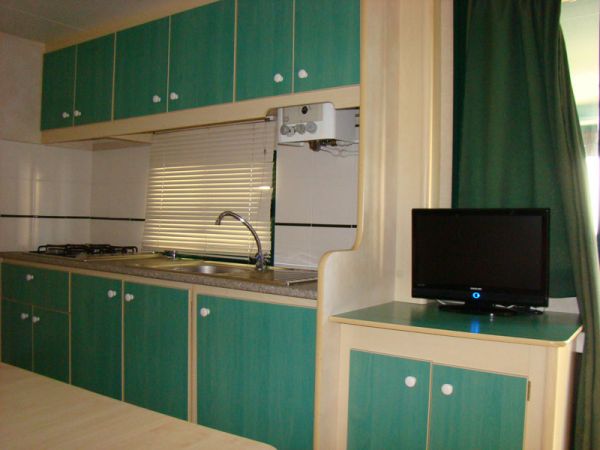 Cucina con mobili verdi, lavello e televisore piccolo.