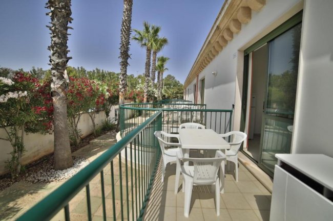 Terrazza balcone con tavolo e sedie bianche, vista su palme e fiori.
