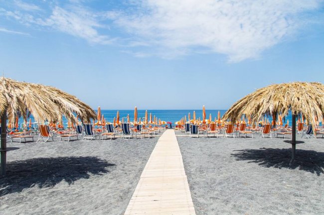 Spiaggia con sedie a sdraio e ombrelloni di paglia, fronte mare.