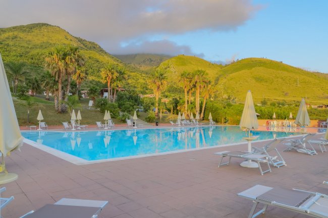 Piscina all'aperto con lettini e vista su colline verdi.