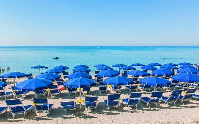 Spiaggia con ombrelloni e sedie blu.
