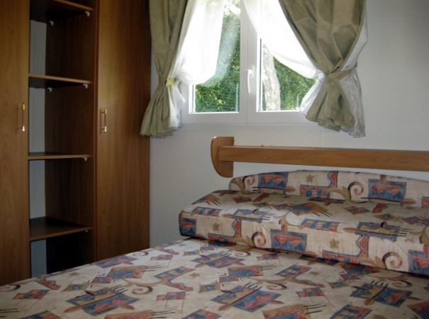 Interno di una camera con letto matrimoniale, armadio e finestre con tende.