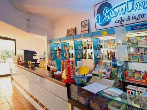 Bancone di un bar con prodotti esposti e una persona dietro il bancone.