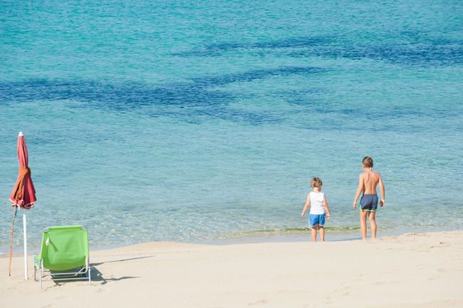 Due bambini sulla riva del mare, sedia e ombrellone sulla sabbia.