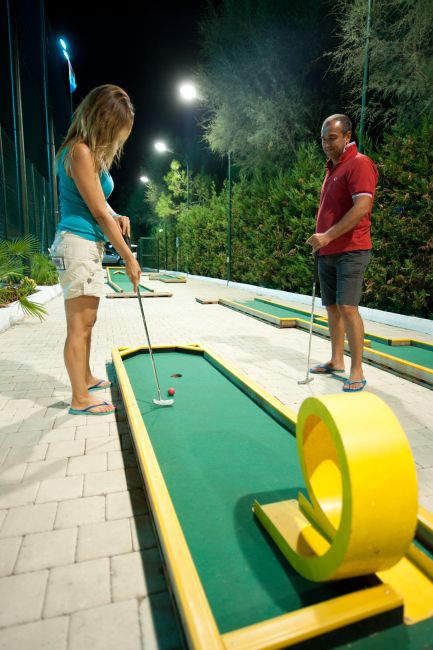 Due persone giocano a minigolf su un percorso illuminato di notte.