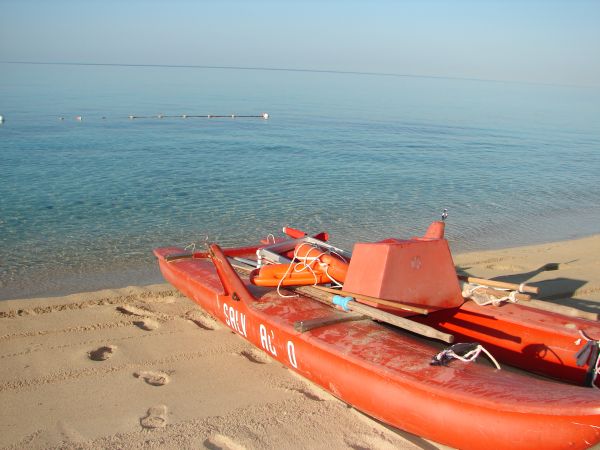 Una barca rossa su una spiaggia di sabbia, con il mare calmo sullo sfondo.