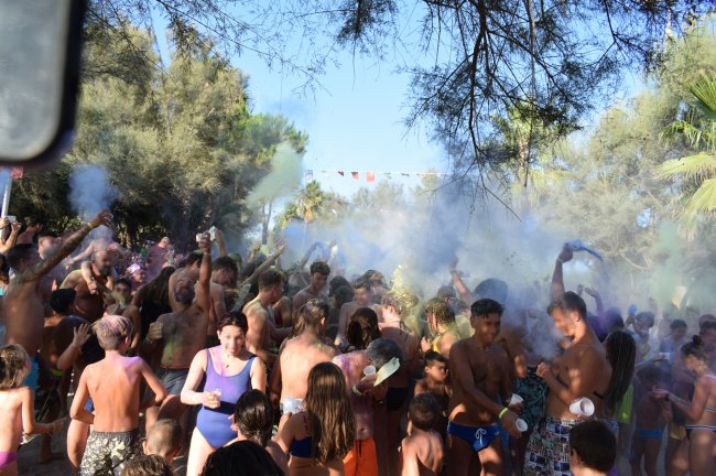Festa con lancio di polveri colorate, persone festanti all'aperto tra gli alberi.