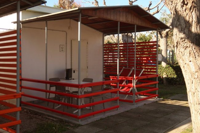 Bungalow bianco con veranda, tavolino e sedie rosse.
