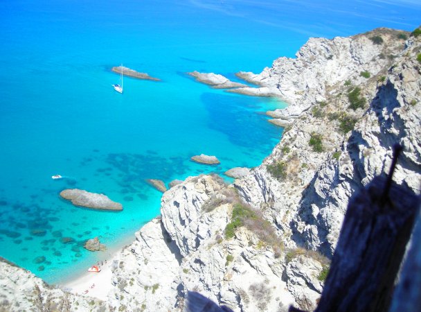 Vista di una scogliera con mare turchese e barche ancorate.