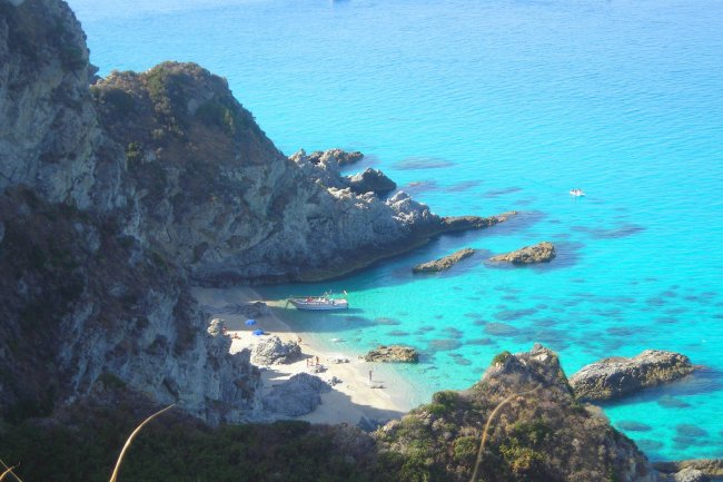 Piccola baia con spiaggia sabbiosa, rocce circostanti e acqua cristallina.