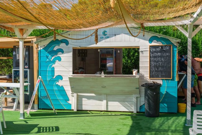 Chiosco con decorazioni a onde blu e menu su lavagna. Due persone accanto.