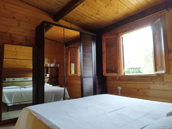 Camera da letto in legno con letto bianco, armadio e finestra aperta.