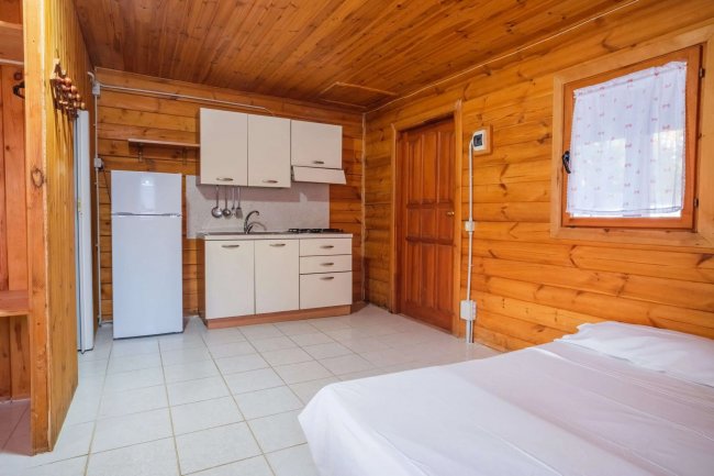 Cucina in legno con frigorifero, armadietti, fornello e letto singolo vicino a una finestra.