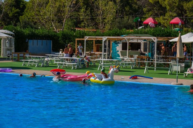 Piscina all'aperto con persone che nuotano e giochi gonfiabili colorati.
