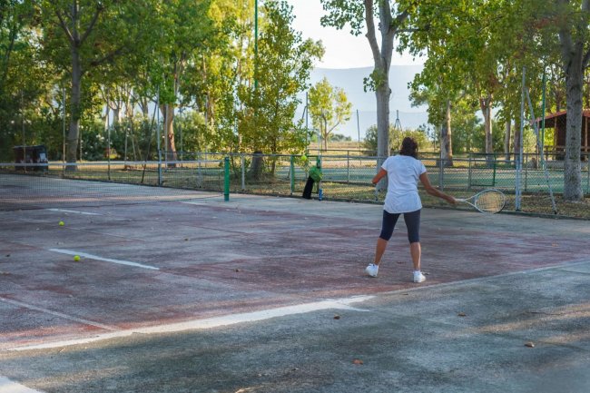 Persona che gioca a tennis su un campo all'aperto circondato da alberi.