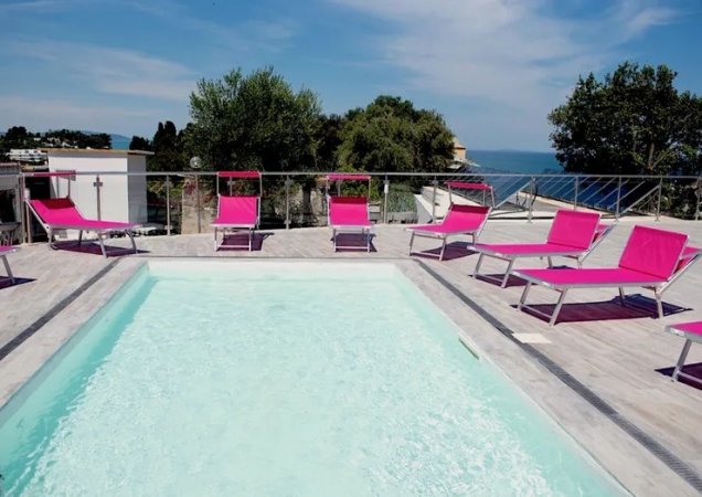 Piscina con lettini rosa e cielo sereno.