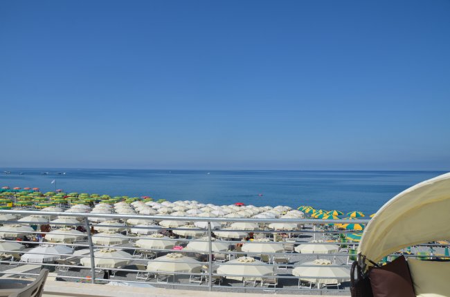 Spiaggia con ombrelloni bianchi e colorati, mare calmo e cielo sereno.