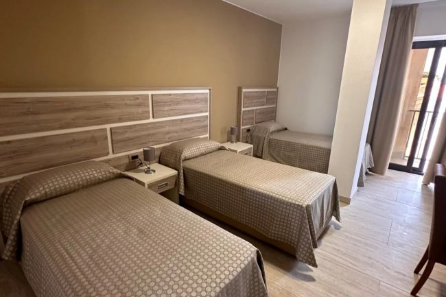 Tre letti singoli in una camera con testiere in legno e parete beige.
