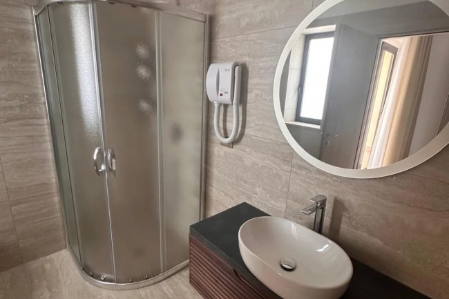 Bagno moderno con doccia angolare, grande specchio rotondo e lavabo bianco.