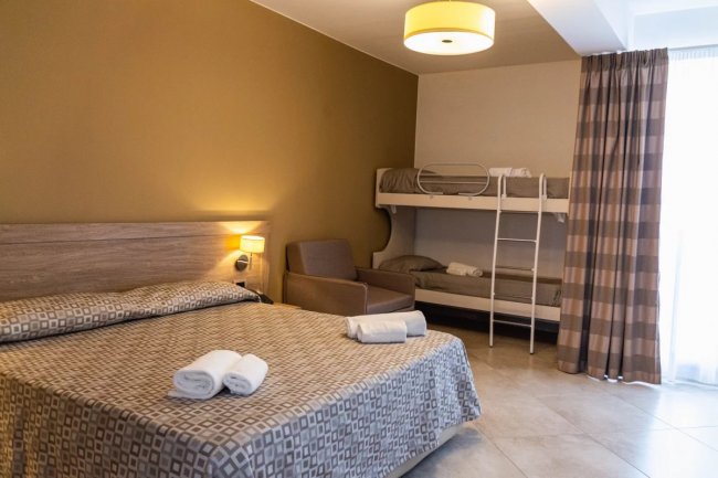 Una camera con letto matrimoniale, letti a castello, poltrona e lampada a soffitto.