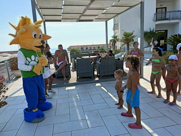 Un personaggio in costume giallo interagisce con bambini su una terrazza soleggiata.