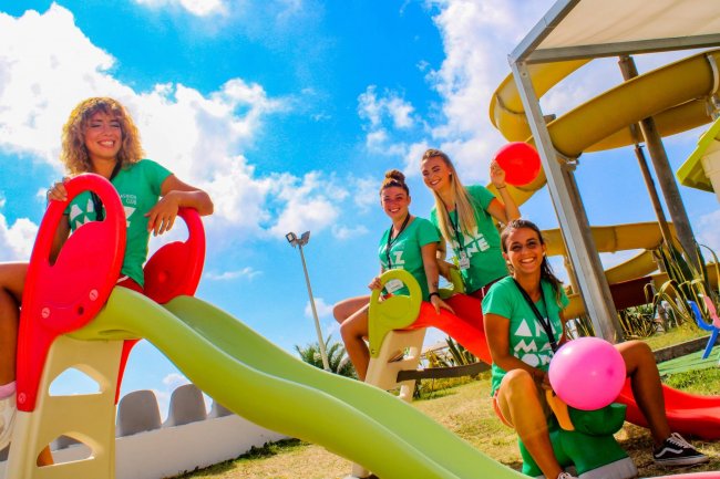 Quattro giovani donne su uno scivolo con palloncini colorati in una giornata soleggiata.
