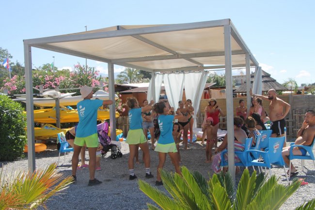 Lezione di fitness all'aperto sotto una tettoia con partecipanti in cerchio.