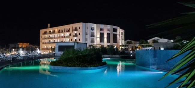 Hotel moderno illuminato di notte, con piscina e area relax.