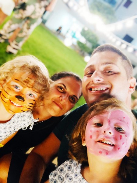 Una famiglia sorride, due bambini con il viso dipinto da tigre e coccinella.