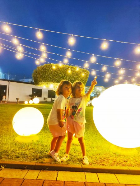 Due bambini in un giardino di sera, circondati da luci decorative.