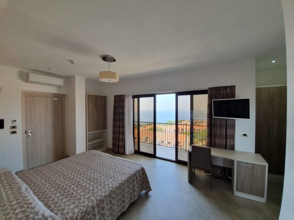 Camera d'albergo moderna con letto matrimoniale, scrivania e balcone vista mare.