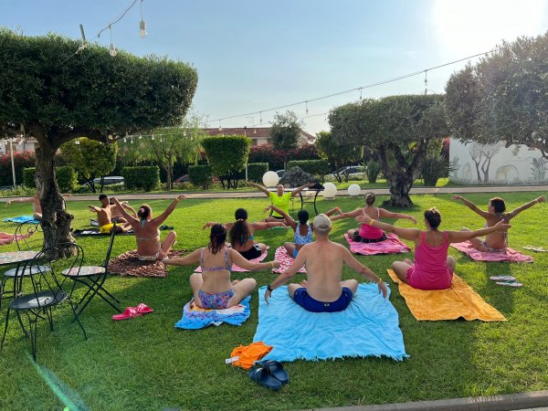 Persone fanno yoga su teli colorati in un giardino verde con alberi intorno.