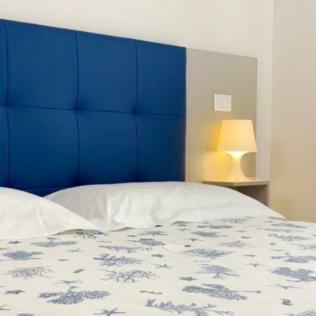Un letto con testiera blu, lampada accesa e copriletto con disegni blu.