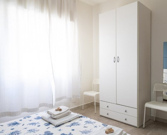 Camera con armadio bianco, tendaggi e letto con copriletto a motivi blu.