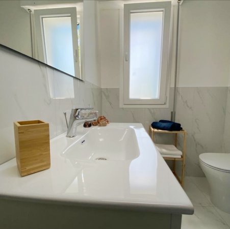 Bagno moderno bianco con lavabo, specchio e finestra.