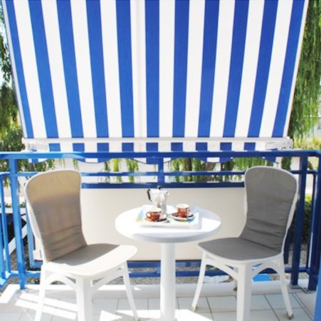 Due sedie e un tavolino bianco su un balcone con tenda a righe blu.