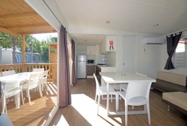 Interno di una casa mobile con tavolo, sedie, cucina e terrazza esterna in legno.