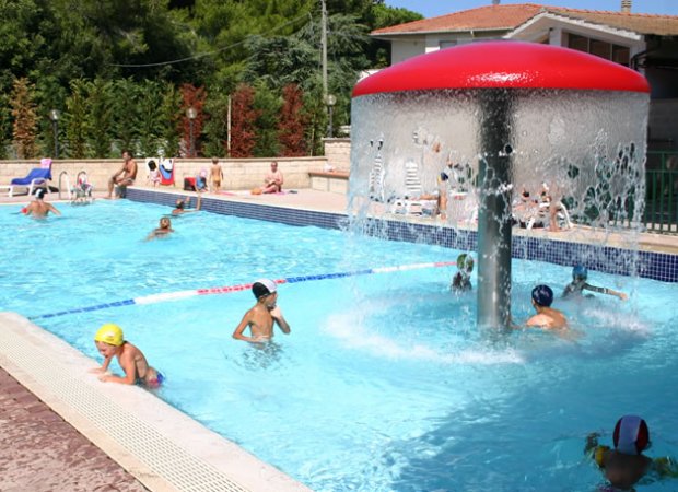 Piscina all'aperto con fontana a forma di fungo e bambini che giocano.