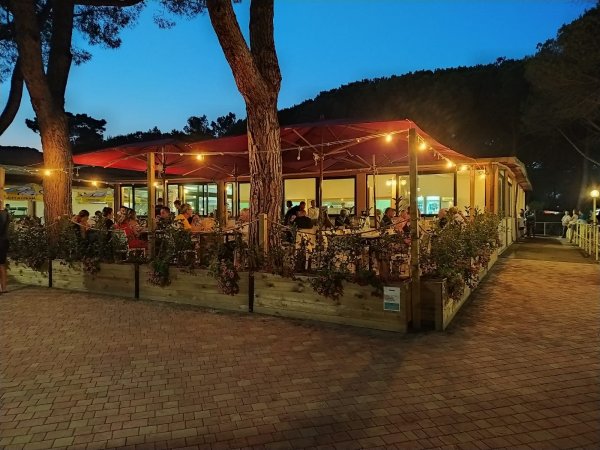 Ristorante all'aperto con tetto rosso, luci soffuse e persone sedute.