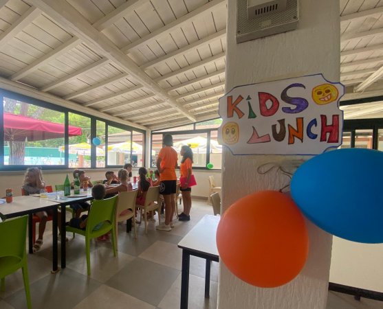 Pranzo per bambini in una sala con decorazioni colorate e animatori.